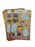 A stack halloween themed sticker sheets on a white background. The stickers feature whimsical illustrations of blue foxes, acorns, a pumpkin, a mushroom, candles, books, and potion bottles on a wood-grain patterned backing.