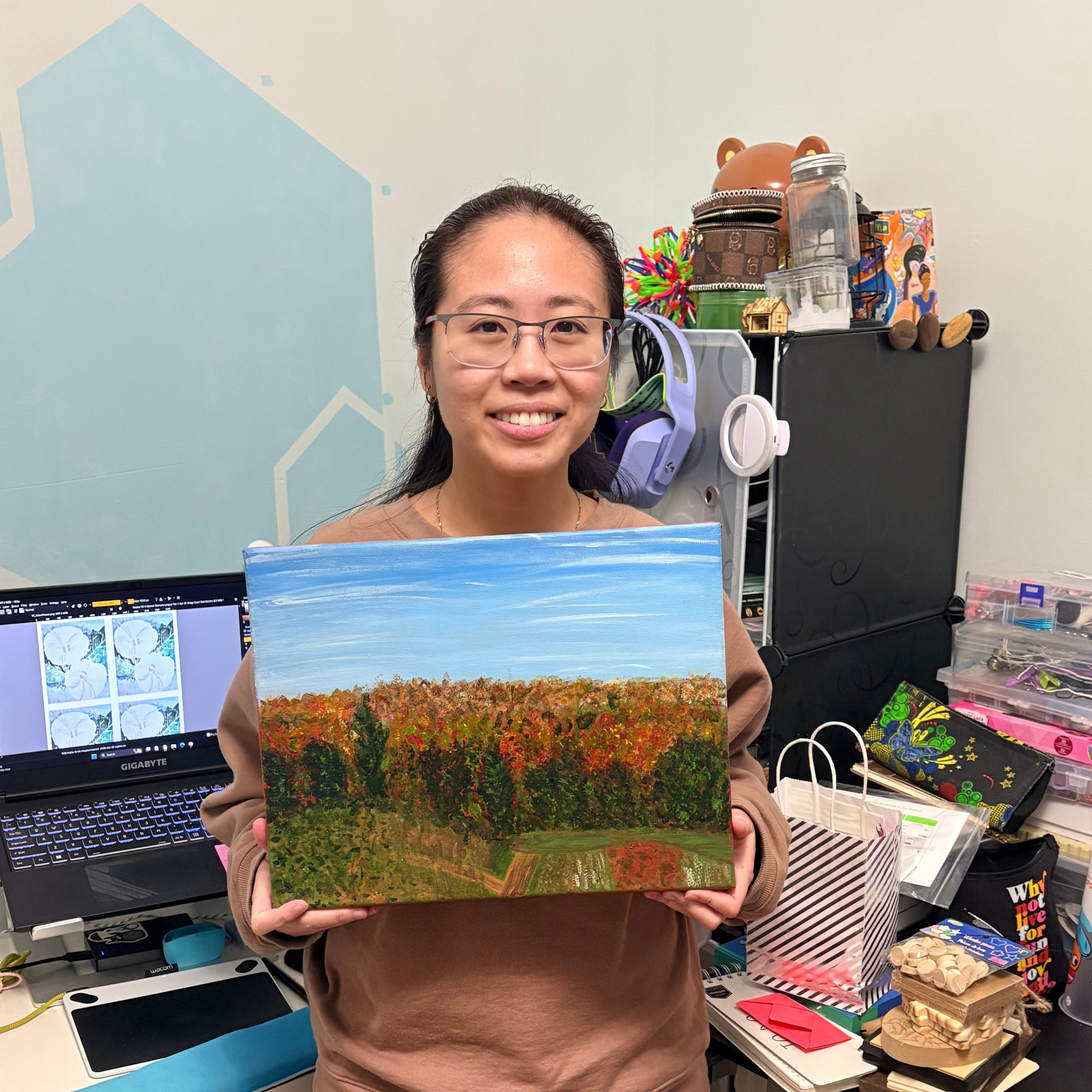 Jessie holding a scenic painting in an office setting