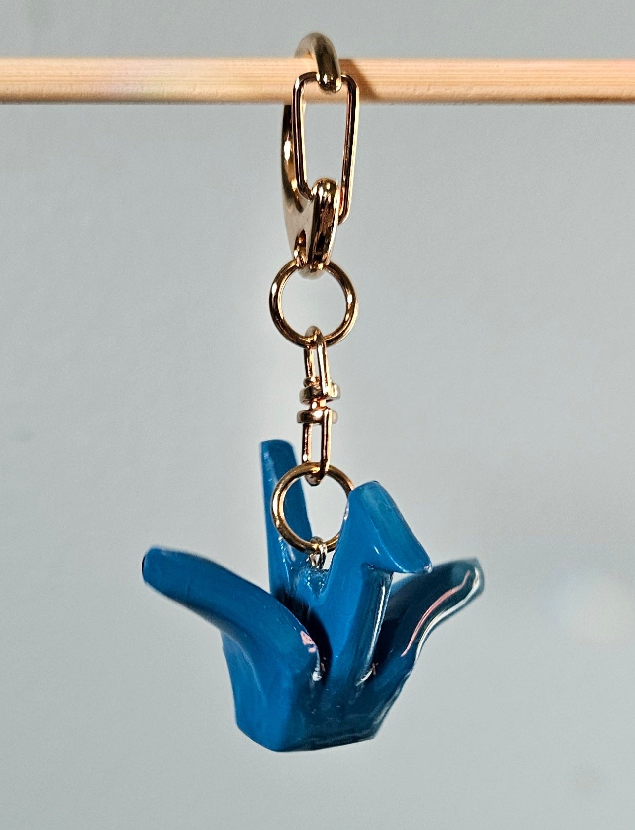 Blue crane-shaped keychain with gold chain on a gray background