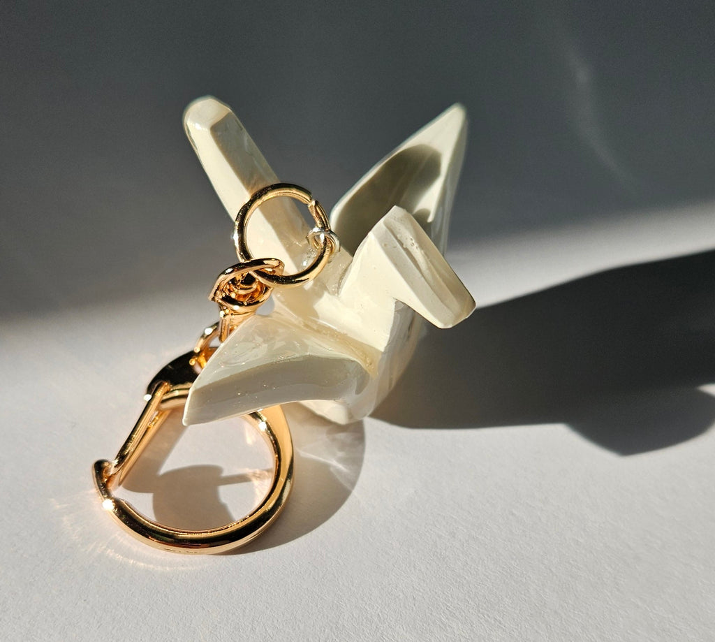White polymer clay crane keychain with a gold D-clasp on a light gray background