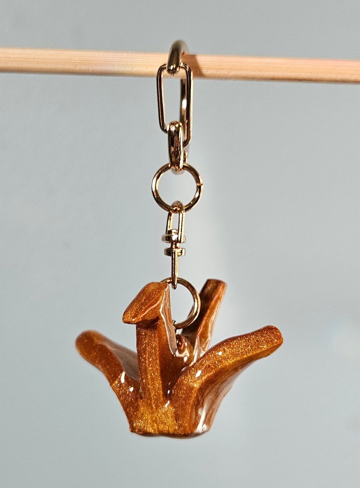 Gold-colored keychain shaped like a crane on a gray background