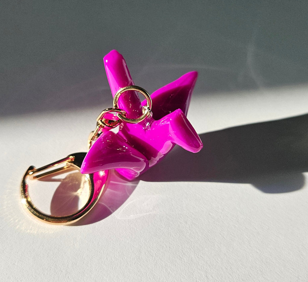 Pink polymer clay crane keychain with gold D-clasp on a light gray background