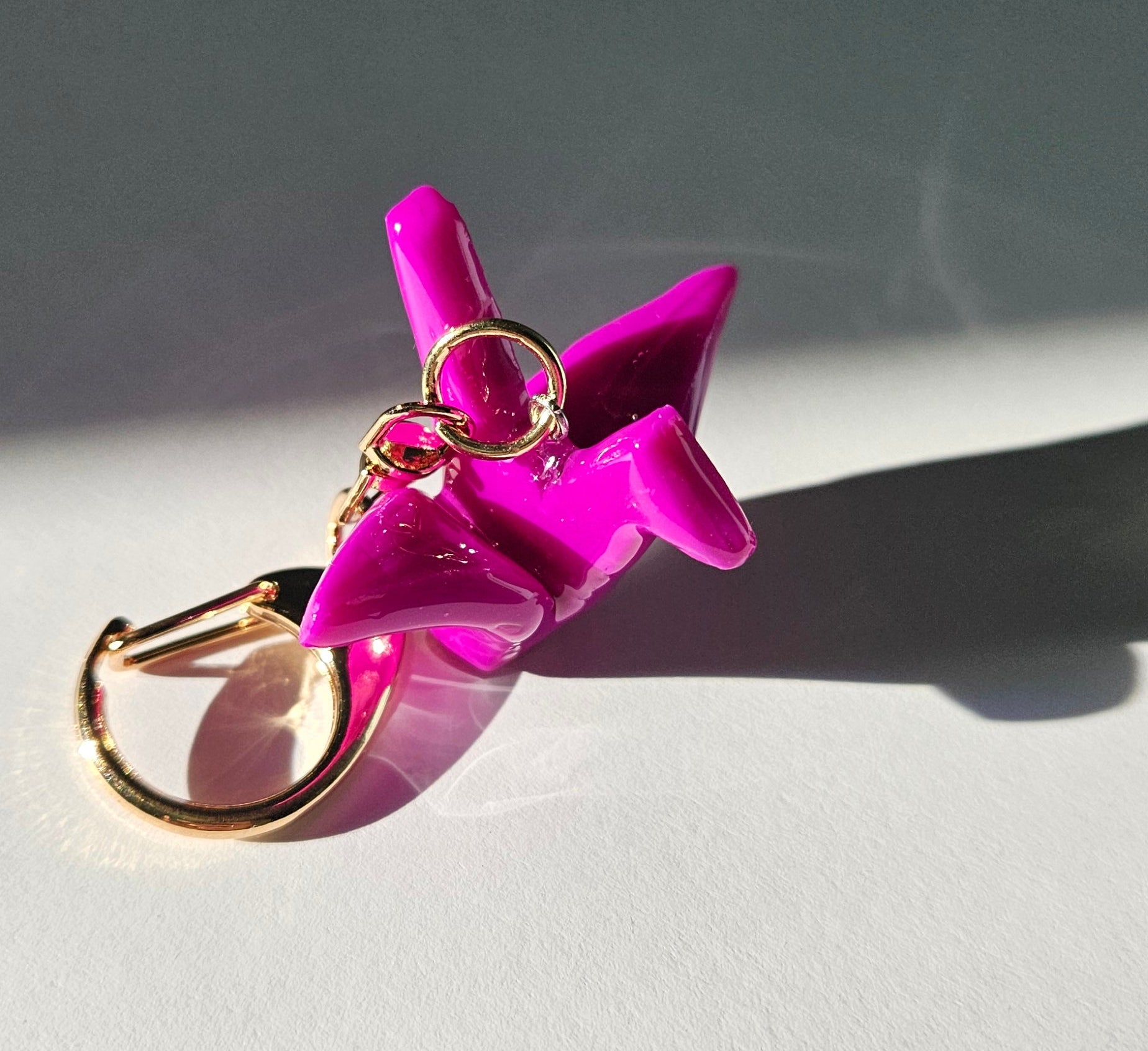Pink polymer clay crane keychain with gold D-clasp on a light gray background