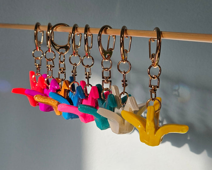 Colorful crane keychainson a stick against a gray background