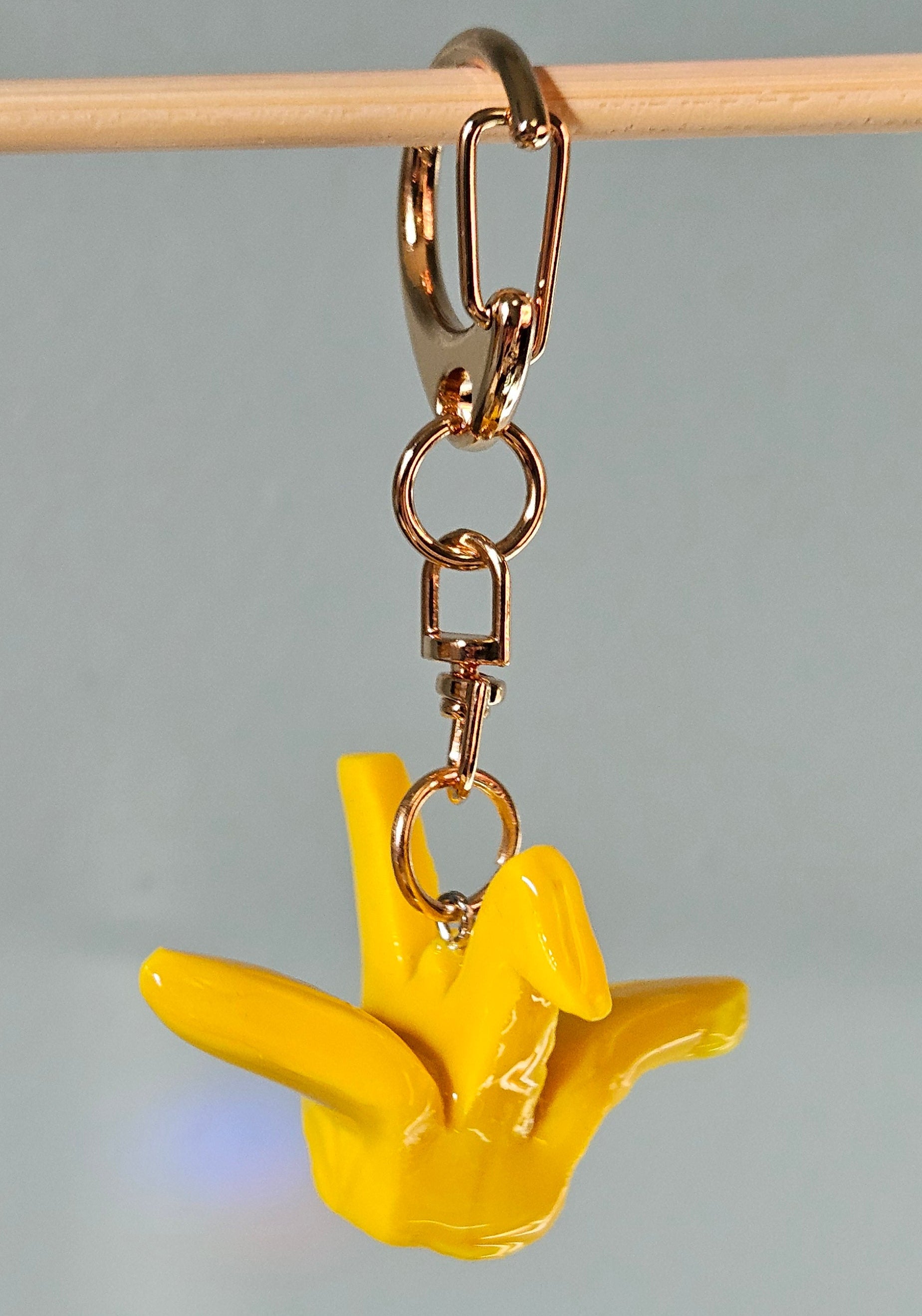 Yellow keychain shaped like a hand making a peace sign on a gray background