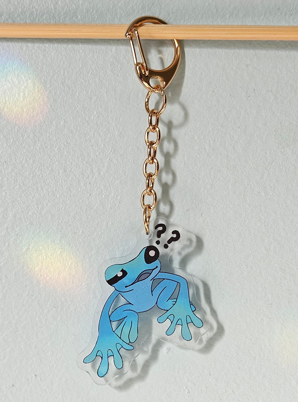 Blue cartoon frog keychain with question marks on a light gray background